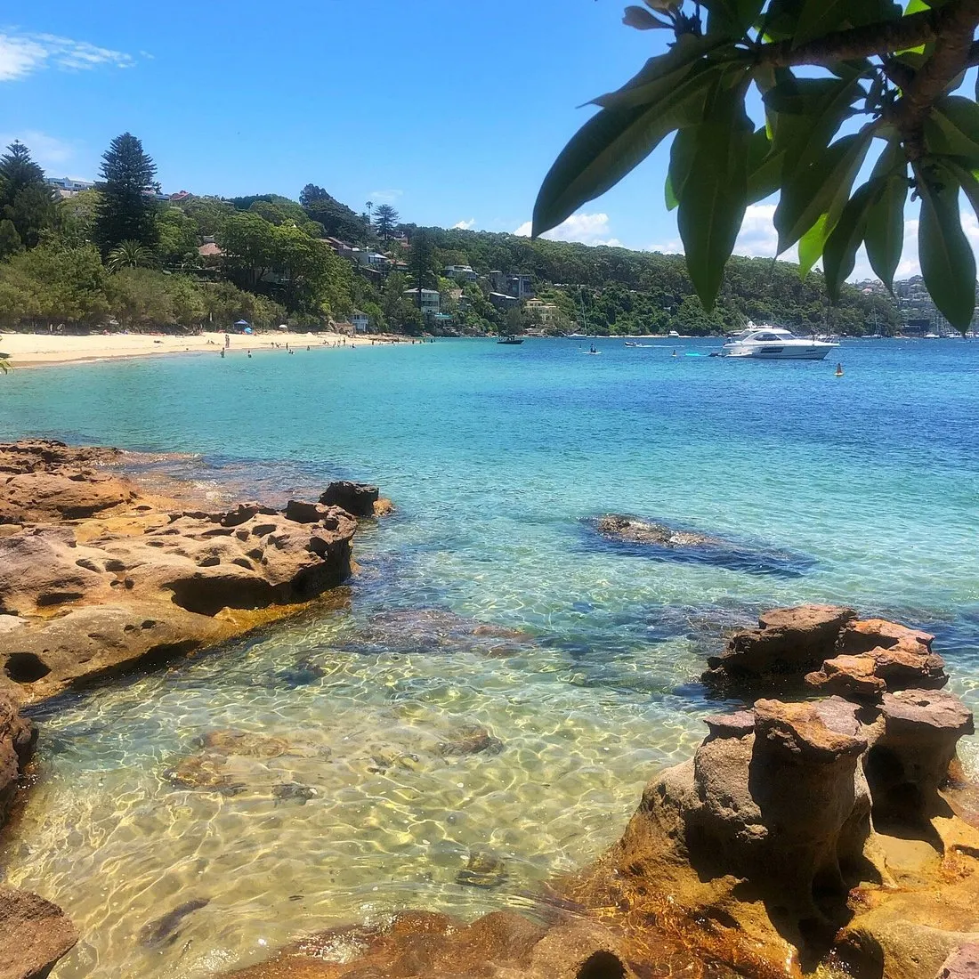 Clear water over sandstone rocks at Chinamans Beach, a motor yacht at anchor off the beach