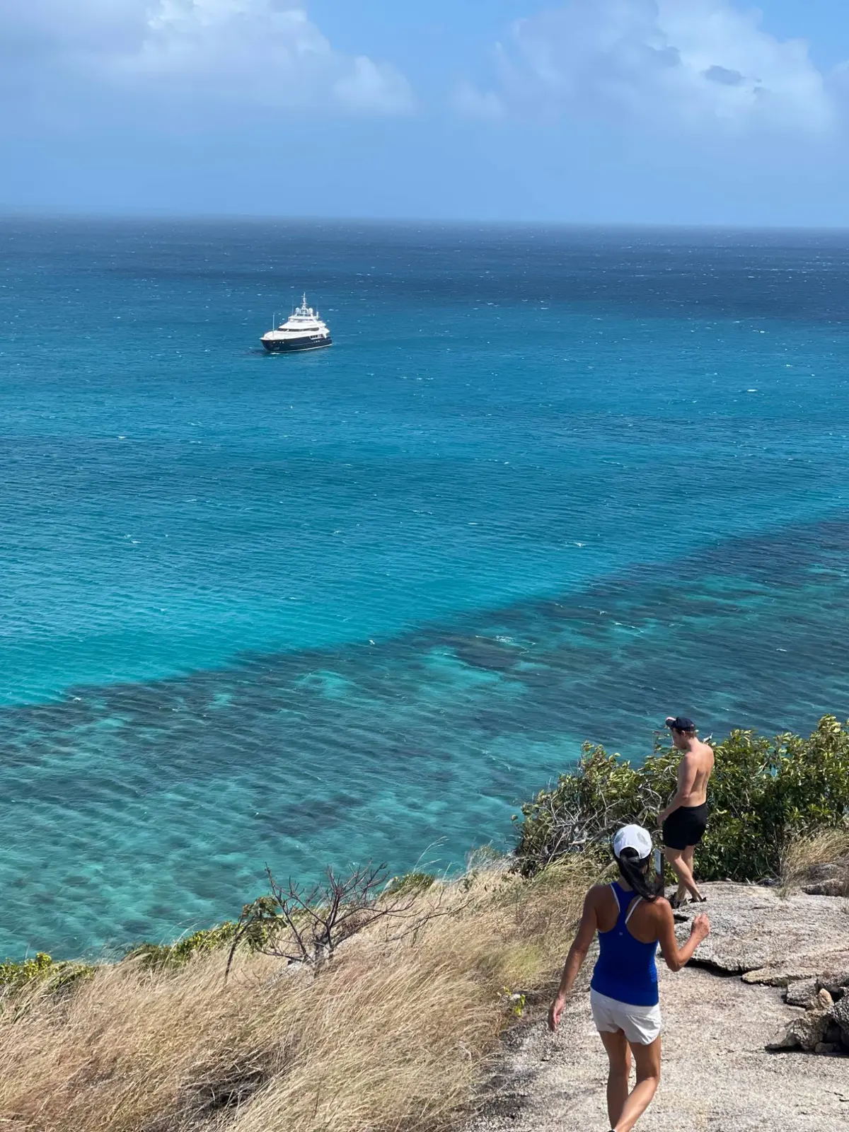 Two guests walking down the Lizard Island lookout track, with the yacht at anchor in turquoise water below