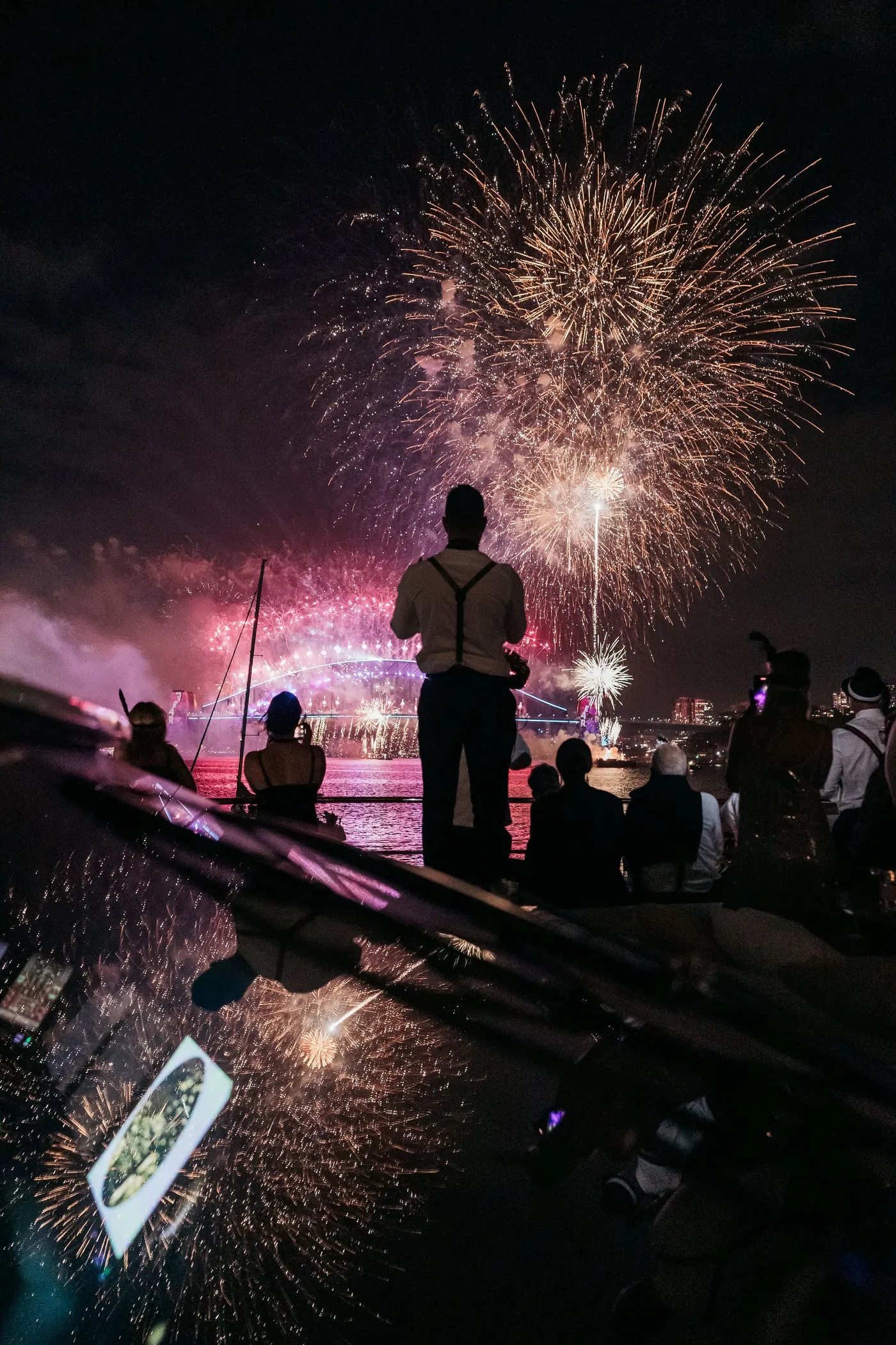 A guest silhouetted on deck against the midnight fireworks over the Harbour Bridge, the show reflected on the yacht