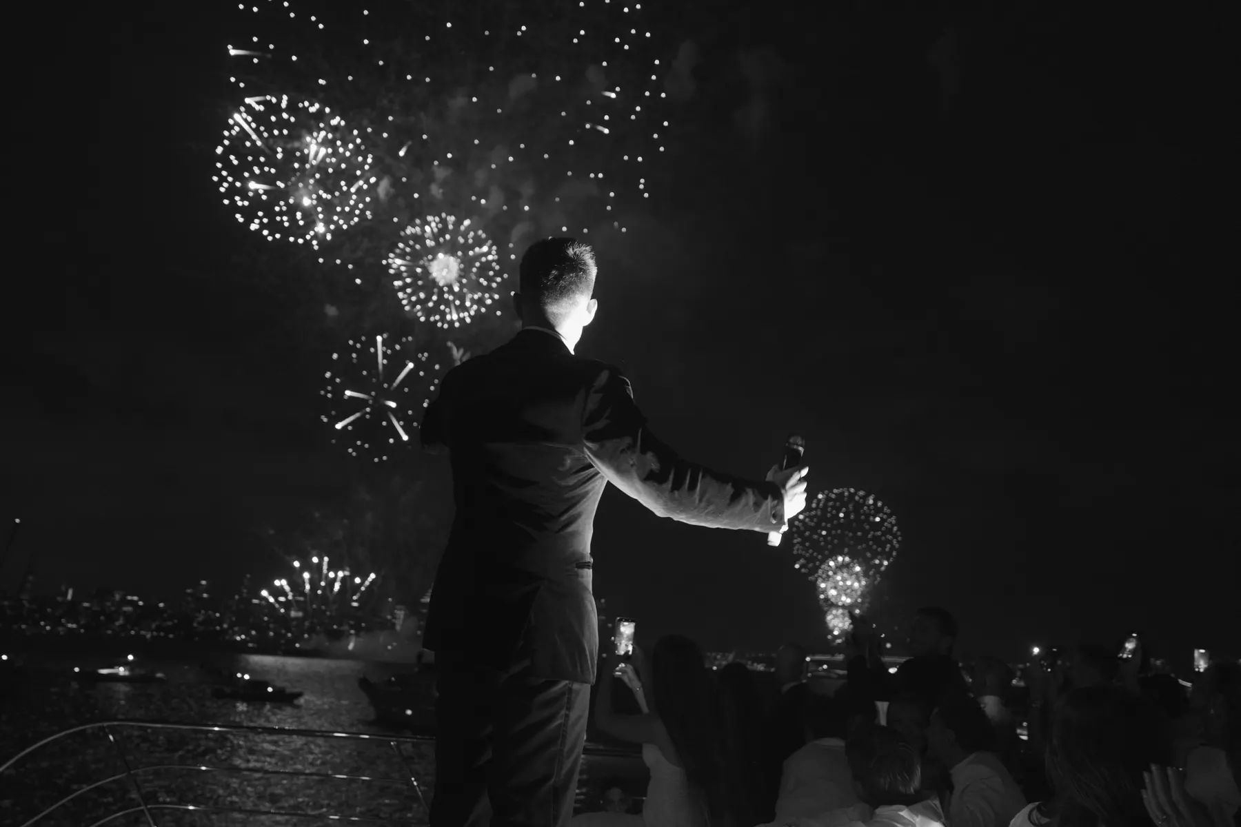 Black and white: a guest raising a microphone to the fireworks over the Harbour, the party behind him