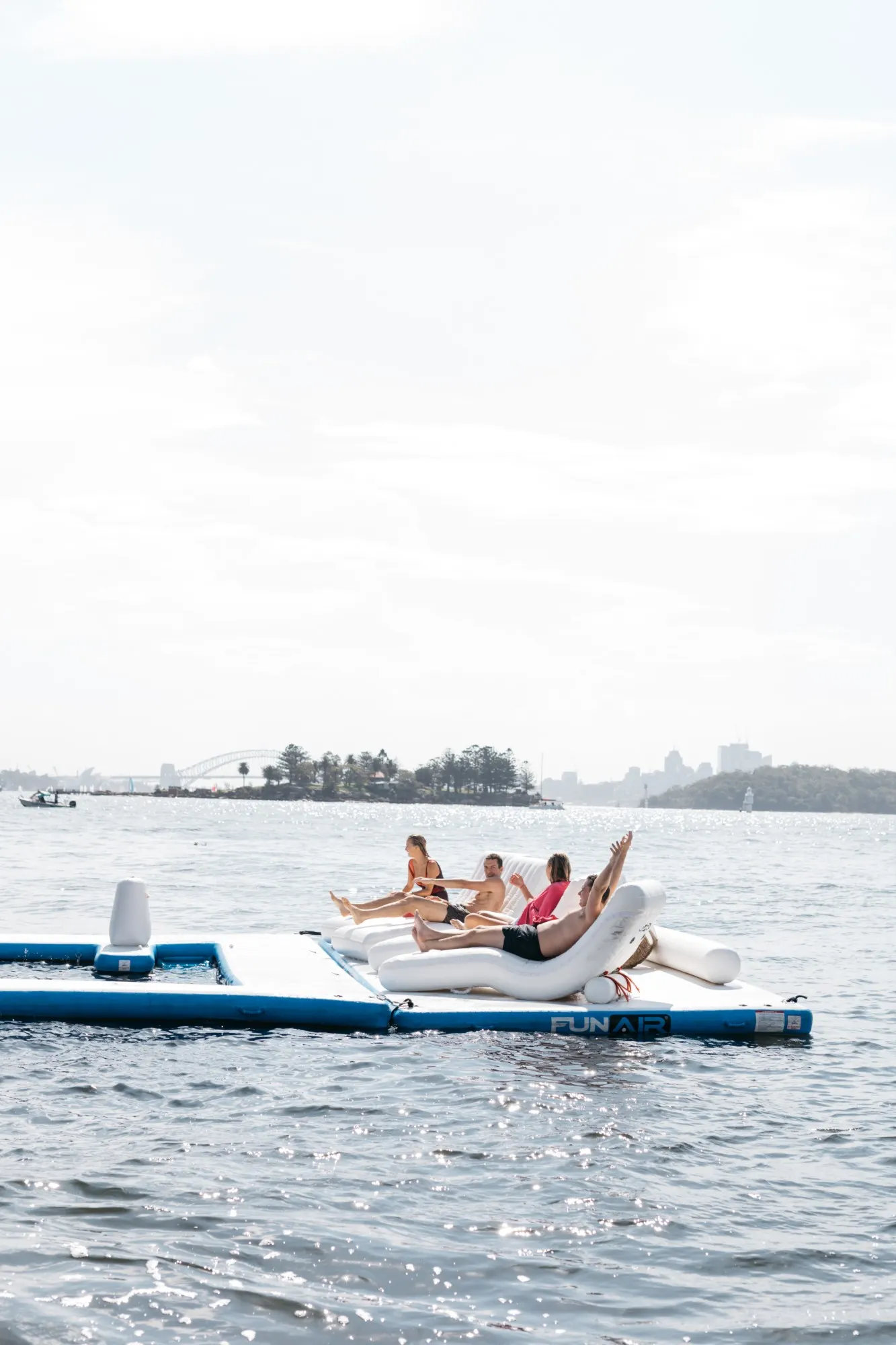 Guests lounging on an inflatable water platform off the yacht on Sydney Harbour, the Bridge in the distance