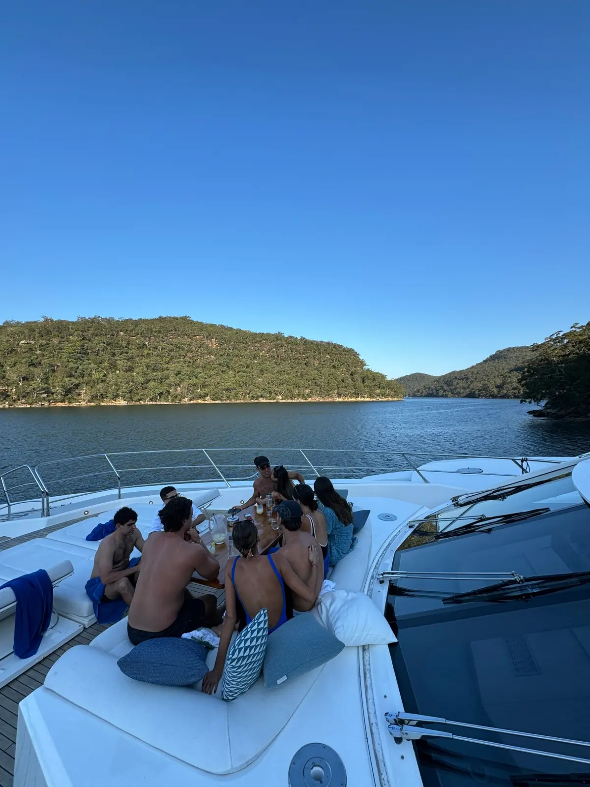 Guests on the bow cushions at anchor in a quiet bushland cove
