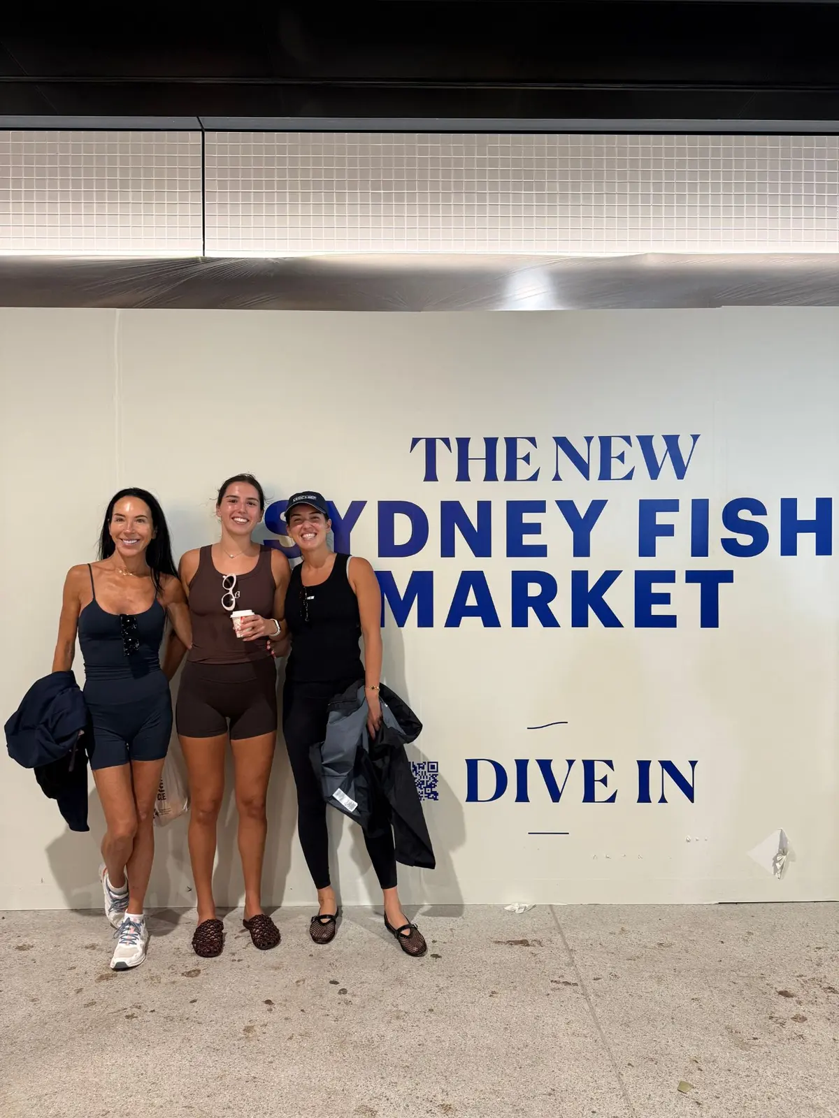 Three of the Ahoy Club team in front of The New Sydney Fish Market sign, one holding a coffee