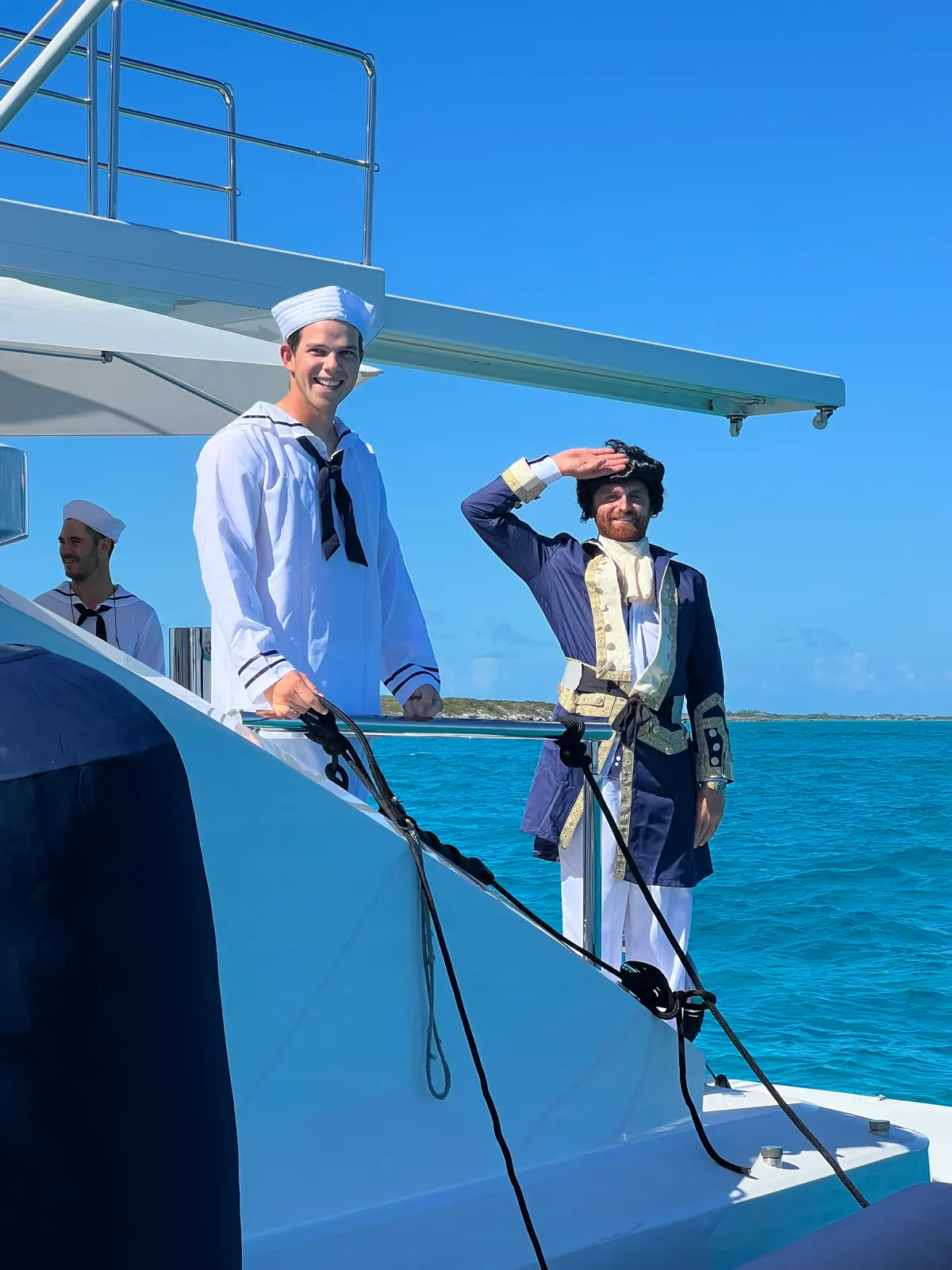 Two of the crew saluting on the bow in sailor whites and a captain's coat